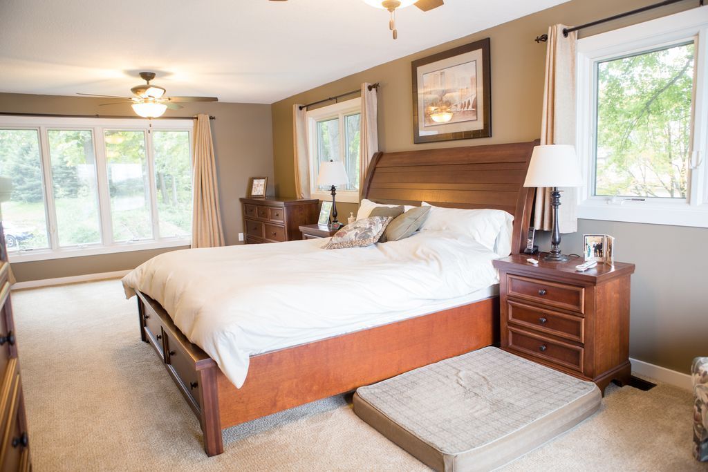 Bedroom with a large wooden bed, bedside tables, and windows with white curtains.