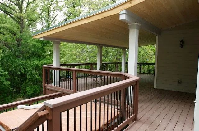 Wooden deck with a covered area, columns, railing, overlooking trees.