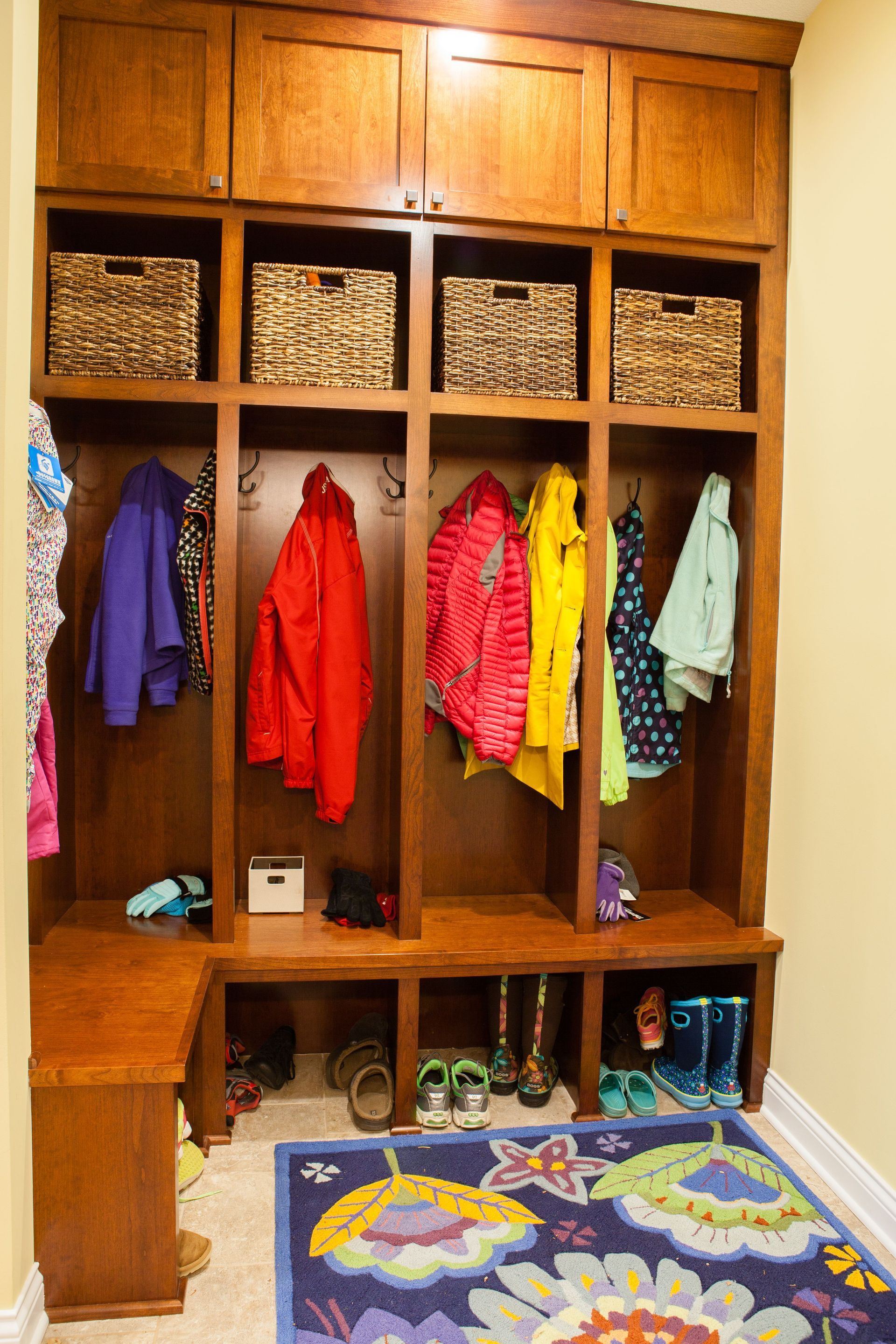 Built-in wooden entry organizer with cubbies, hanging space, and shoe storage, holding coats, baskets, and shoes.