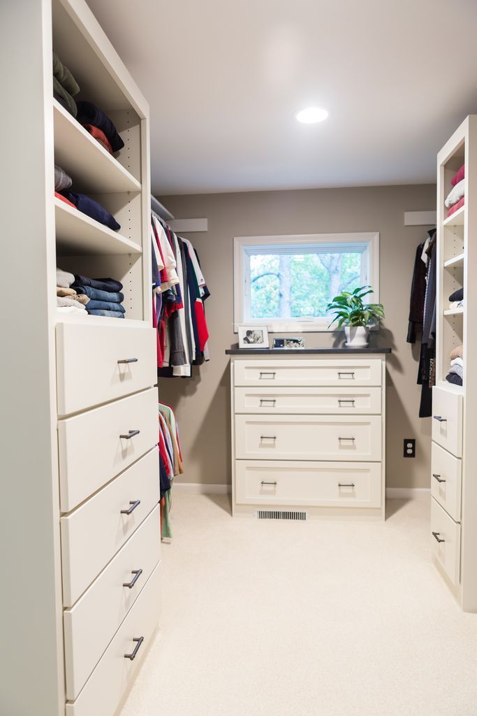 Walk-in closet with white cabinetry, drawers, and hanging rods; a window provides natural light.