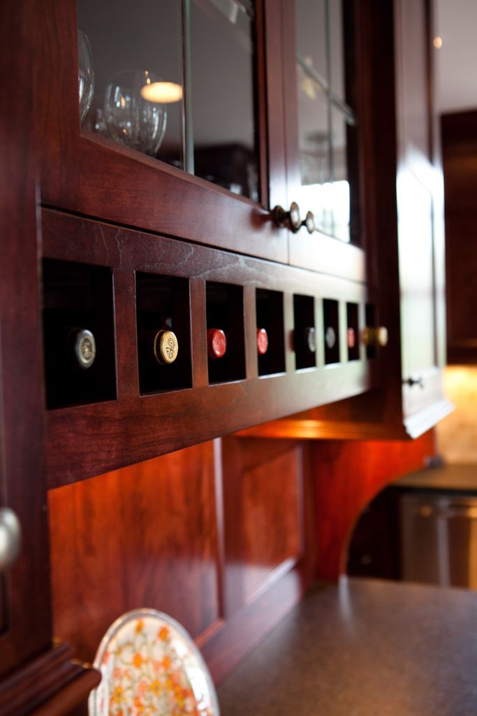 Dark wood wine rack built into kitchen cabinet, holding several bottles.