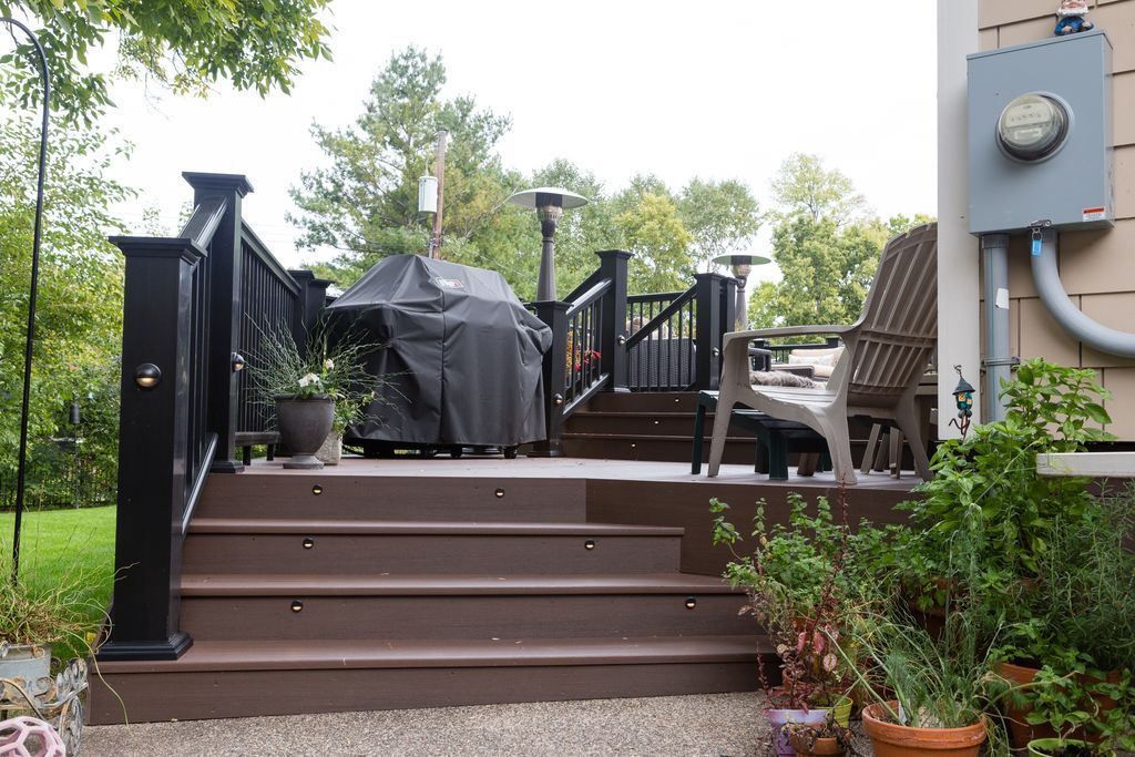 Brown deck with black railings, grill, and seating next to a house.