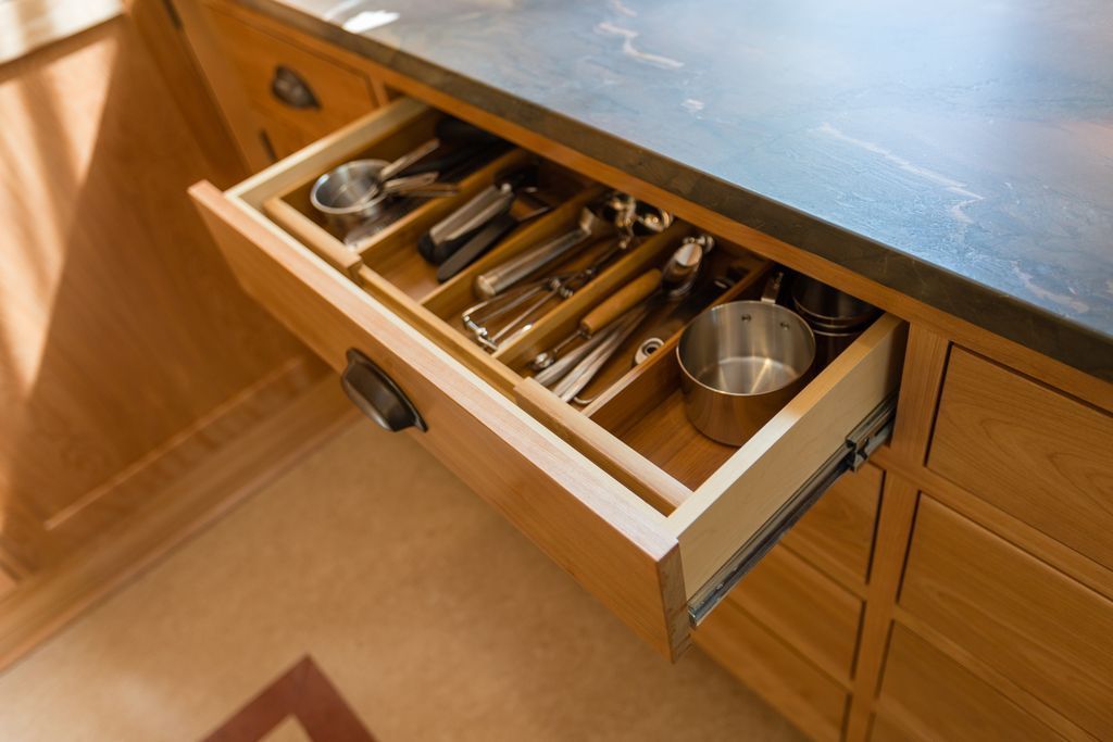 Open wooden kitchen drawer with utensils in a divided organizer; countertop above.