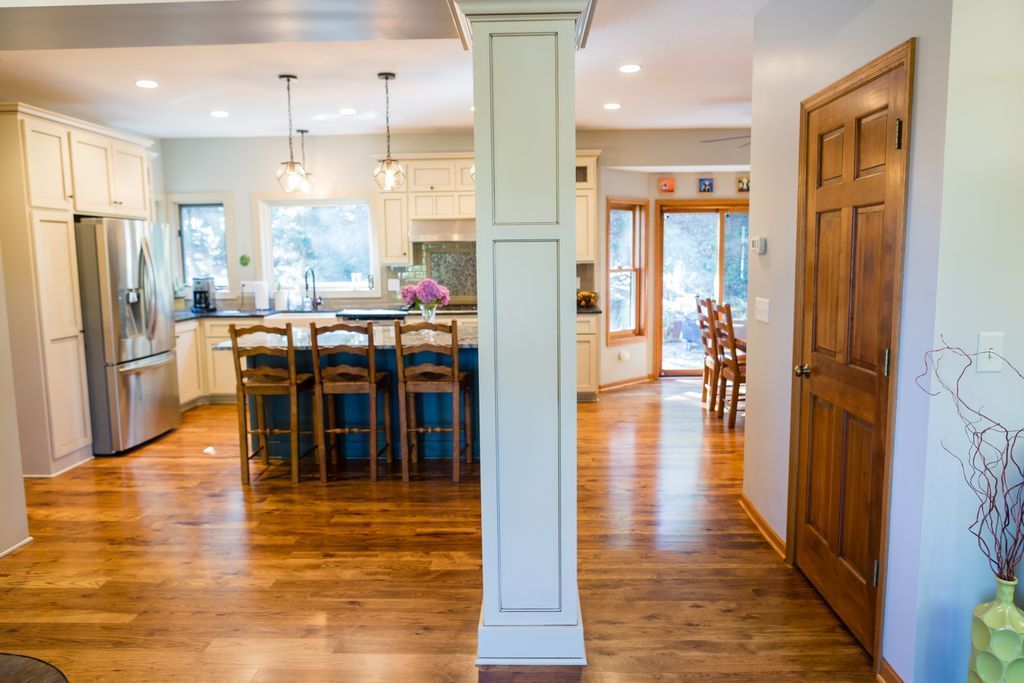 Spacious kitchen with island and bar seating, wood floors, a central white pillar, and an adjacent hallway.