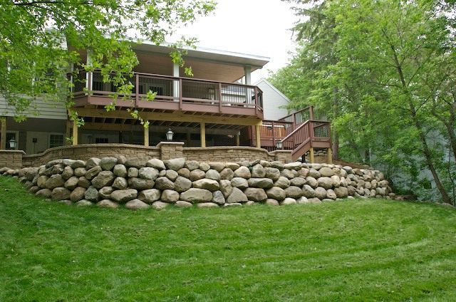 Stone retaining wall supports a deck on a house with green lawn and trees.