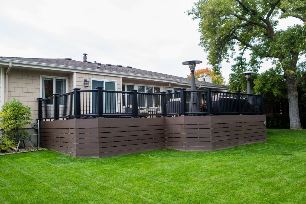 A backyard deck with black railings, brown siding, and a green lawn. House is visible in background.