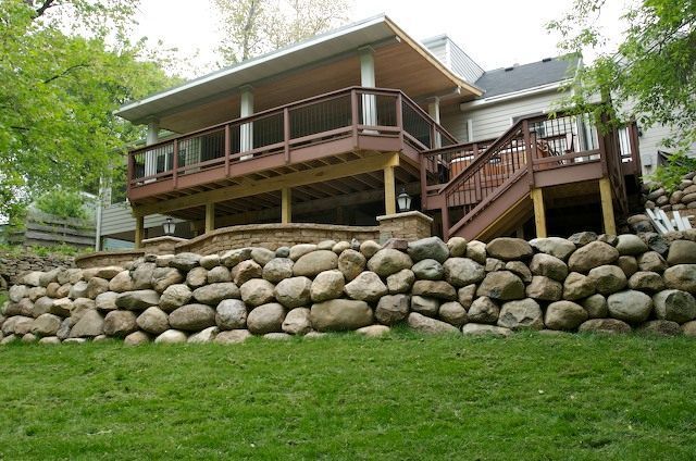 Stone retaining wall supports a two-story deck attached to a house.