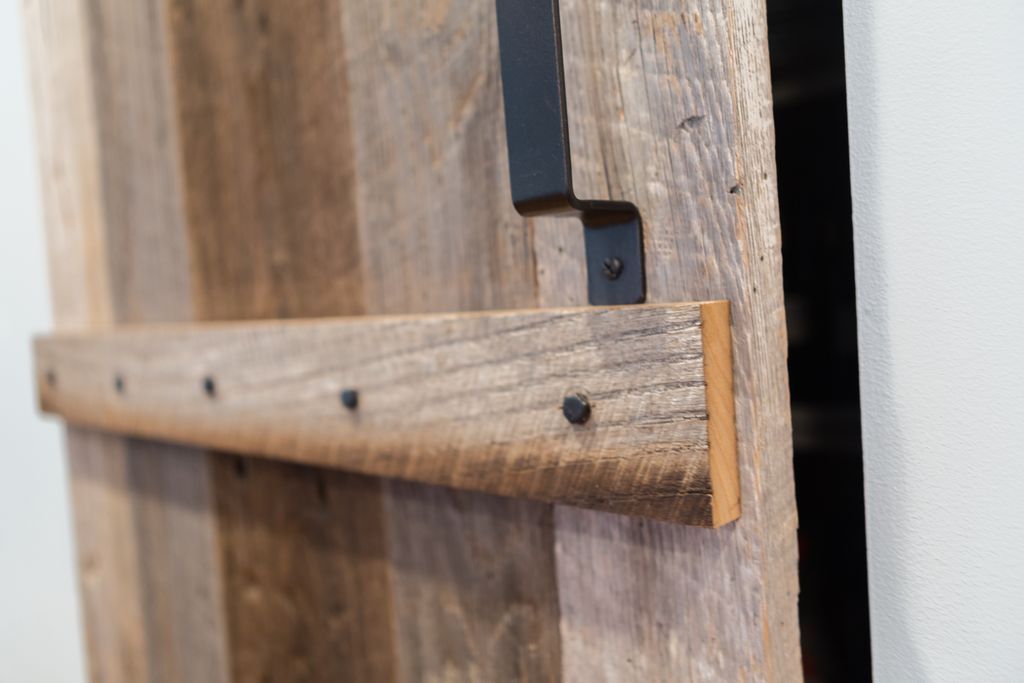 Close-up of a weathered wooden door with a black metal handle and horizontal wooden bar secured with dark nails.