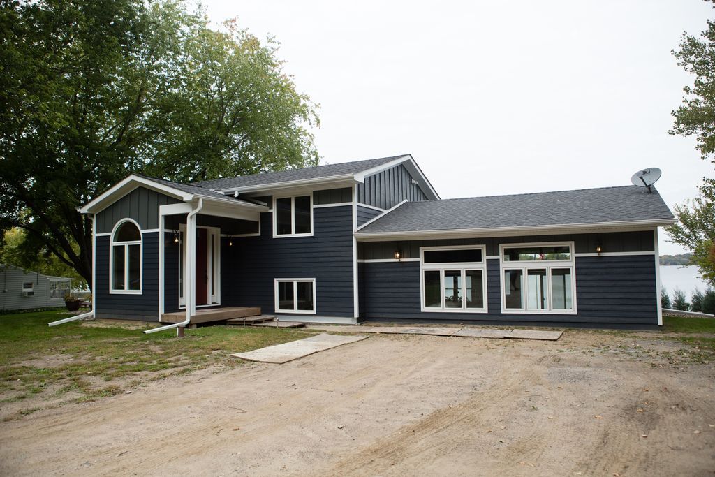 Dark blue house with white trim, gravel driveway, and waterfront in the background.