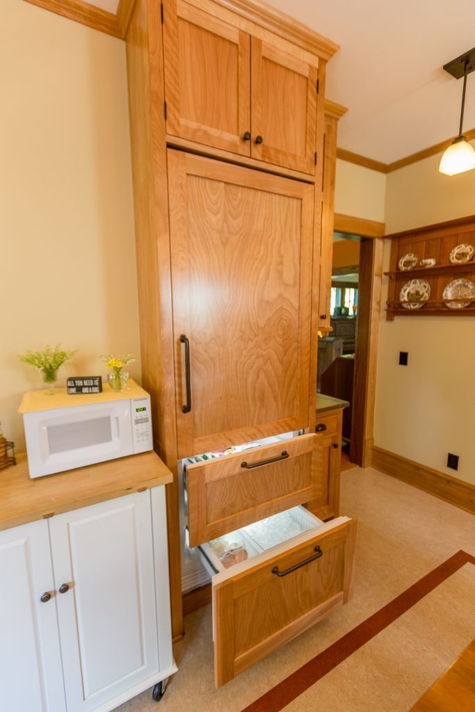 Tall, wooden built-in refrigerator with opened drawers in a kitchen setting, alongside a microwave on a white cabinet.