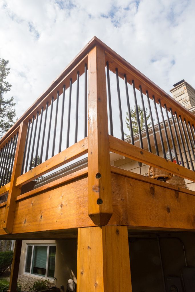 Wooden deck with black metal railings against a cloudy sky.