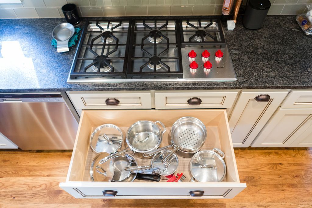 Open kitchen drawer with stainless steel pots and lids below a gas stove.