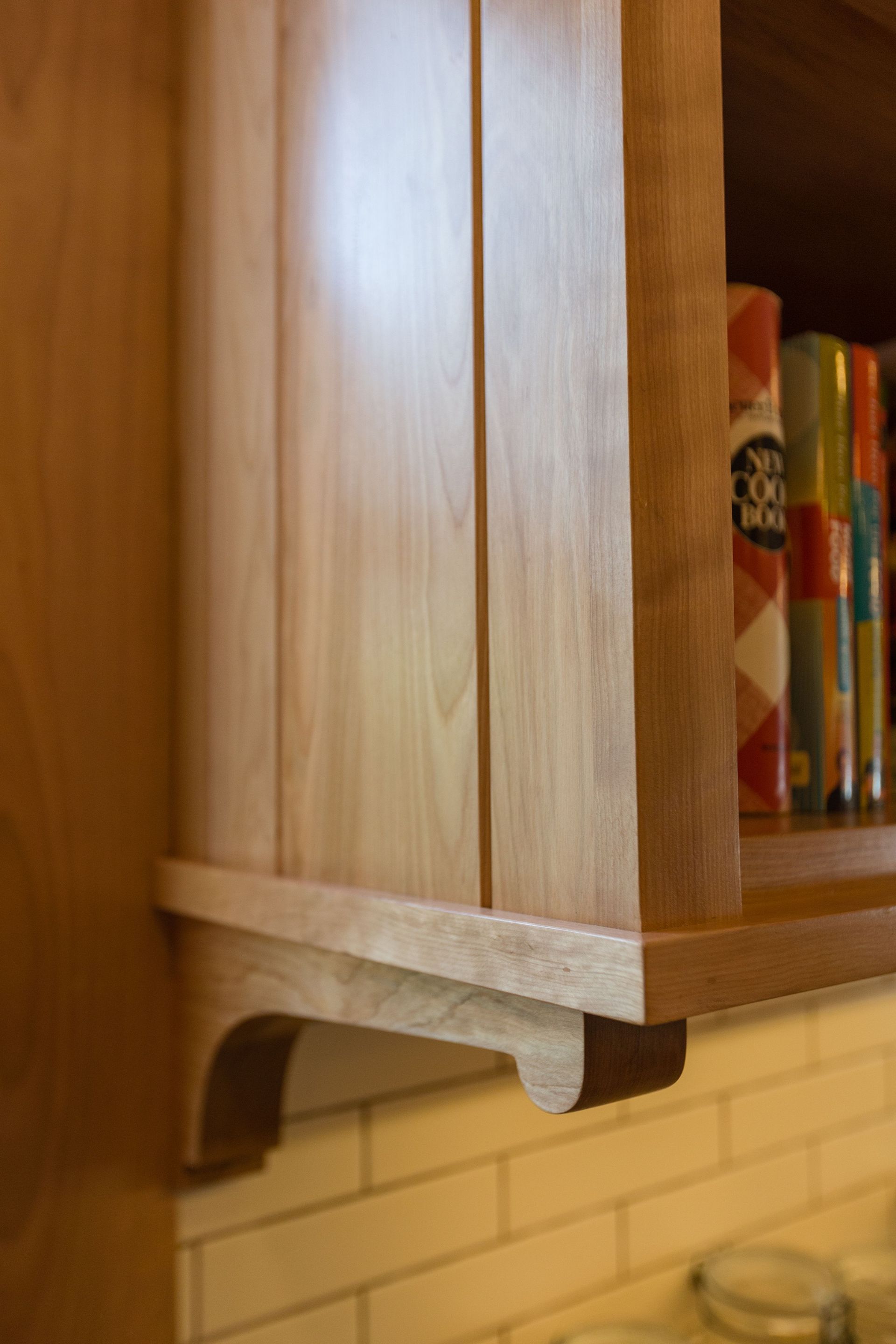 Wooden cabinet with shelf holding books, light wood, angled support bracket.