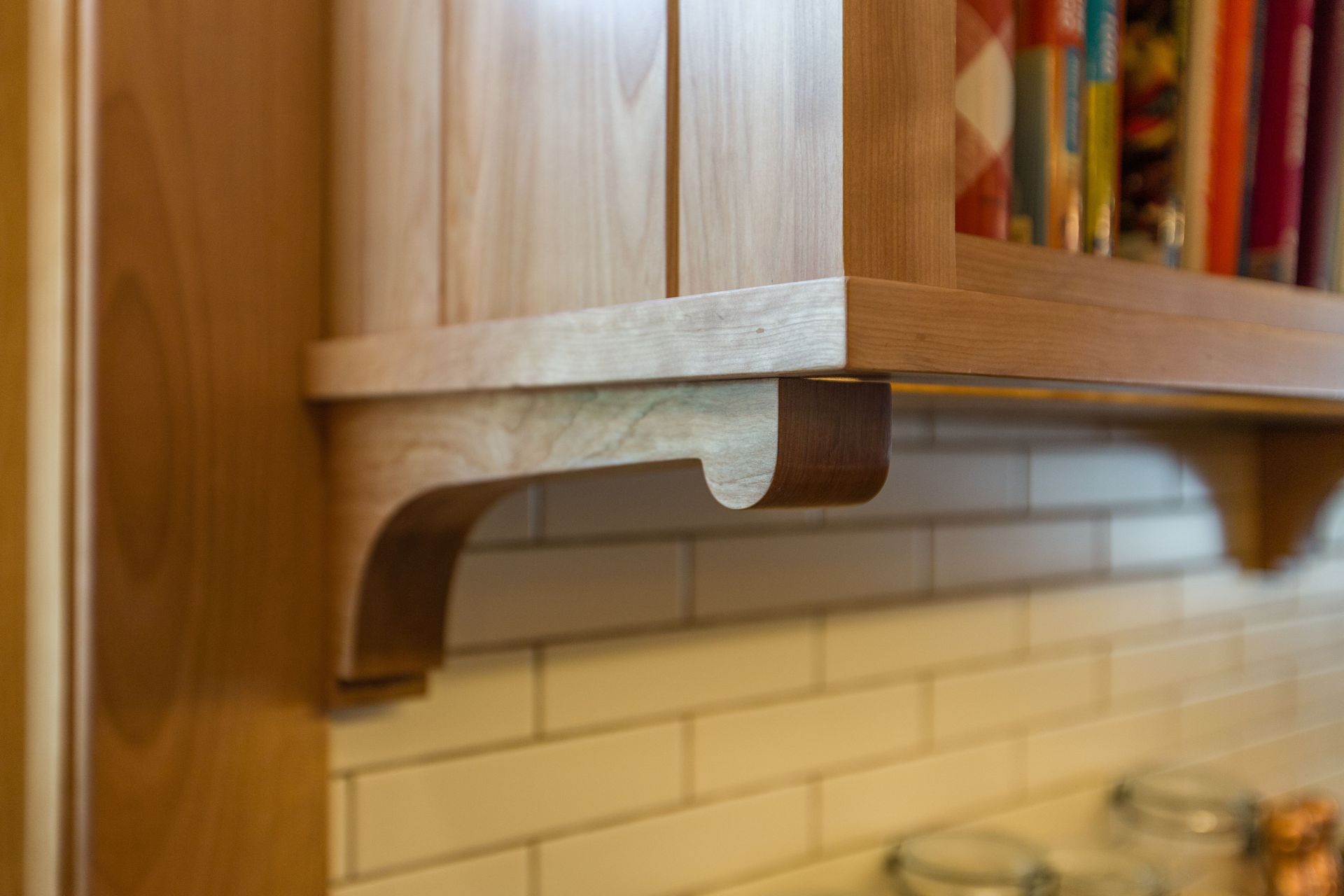 Wooden cabinet detail: A shelf with curved support, light wood against white tile backsplash.