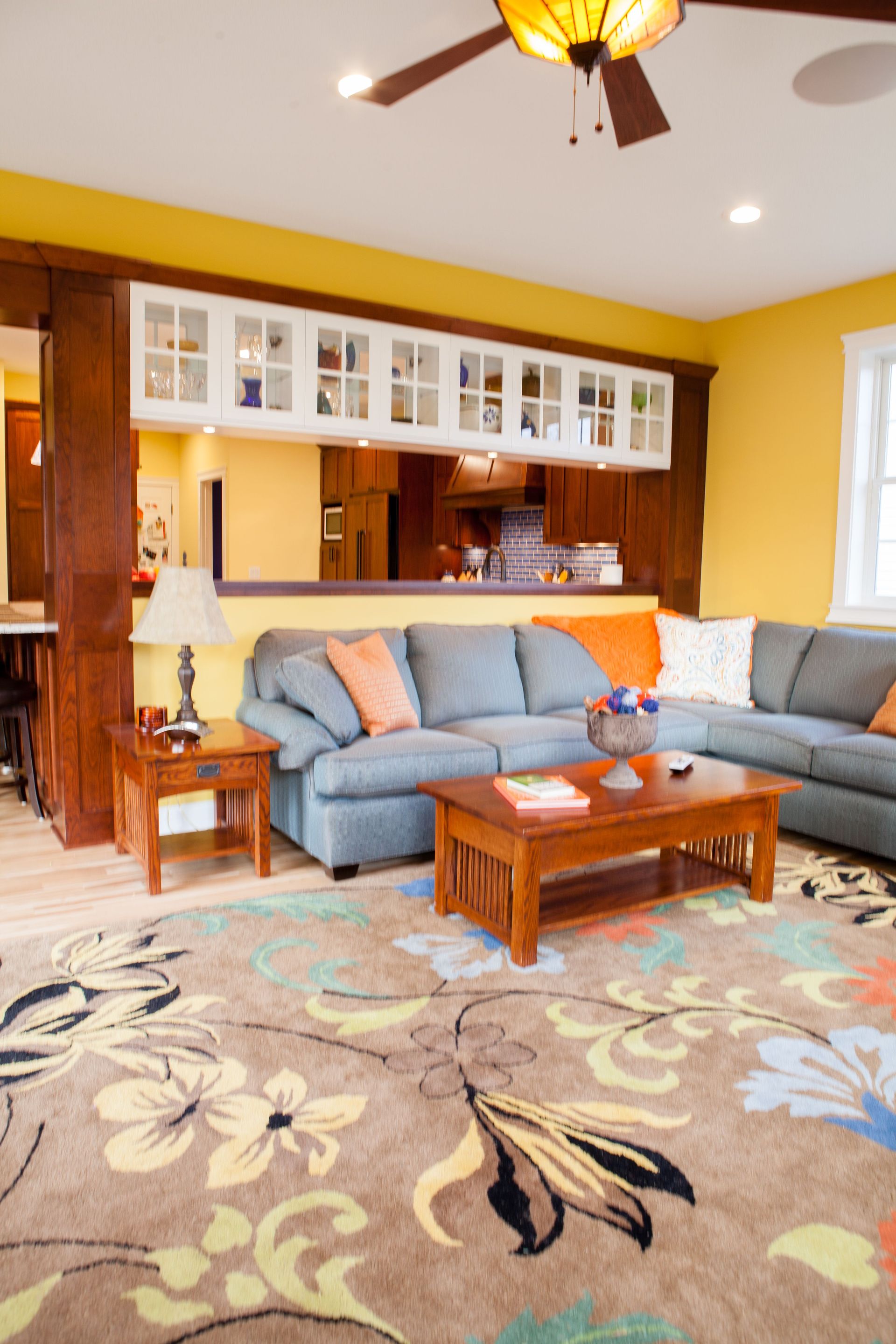 Living room with blue sectional sofa, floral rug, wooden furniture, yellow walls.