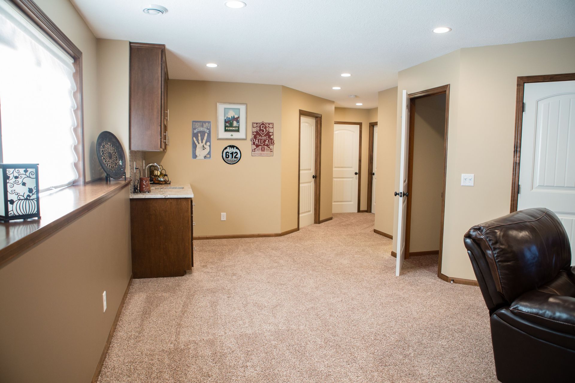 Beige carpeted room with cabinets, doors, and a leather armchair; natural light.