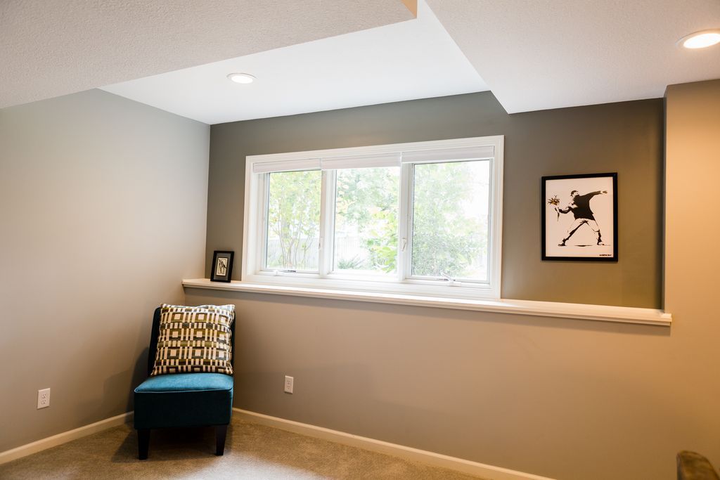 A window seat with a chair, art, and a pillow in a room with neutral-toned walls.