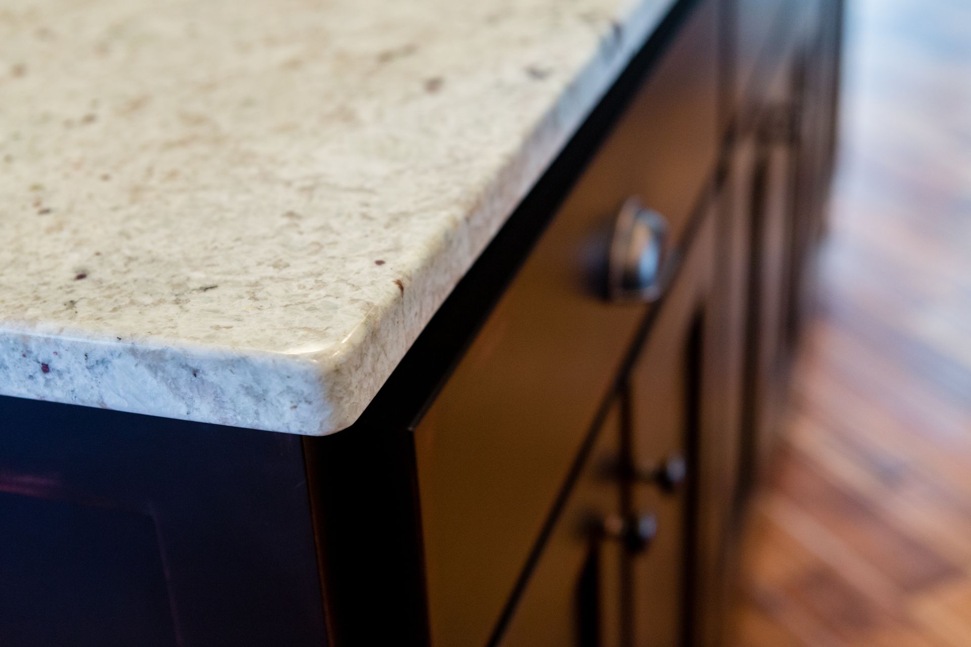 Close-up of a light speckled granite countertop on a dark wood cabinet with a drawer pull.