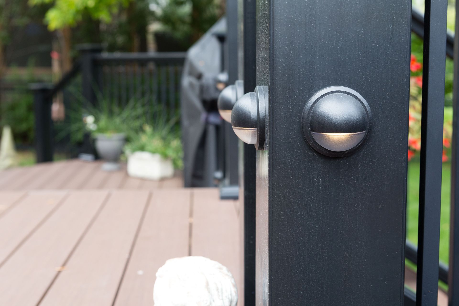Black deck post with installed lights. Brown deck boards lead to a green background.