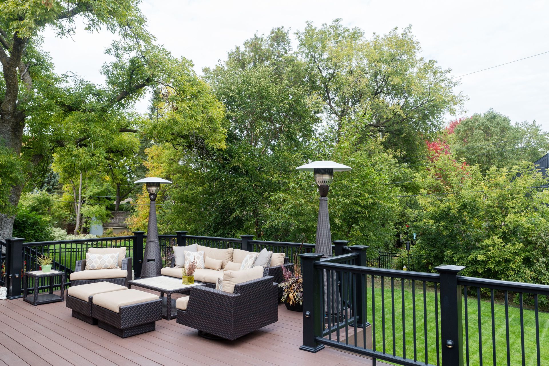 Deck with outdoor seating, gas heaters, and lush green trees in the background.