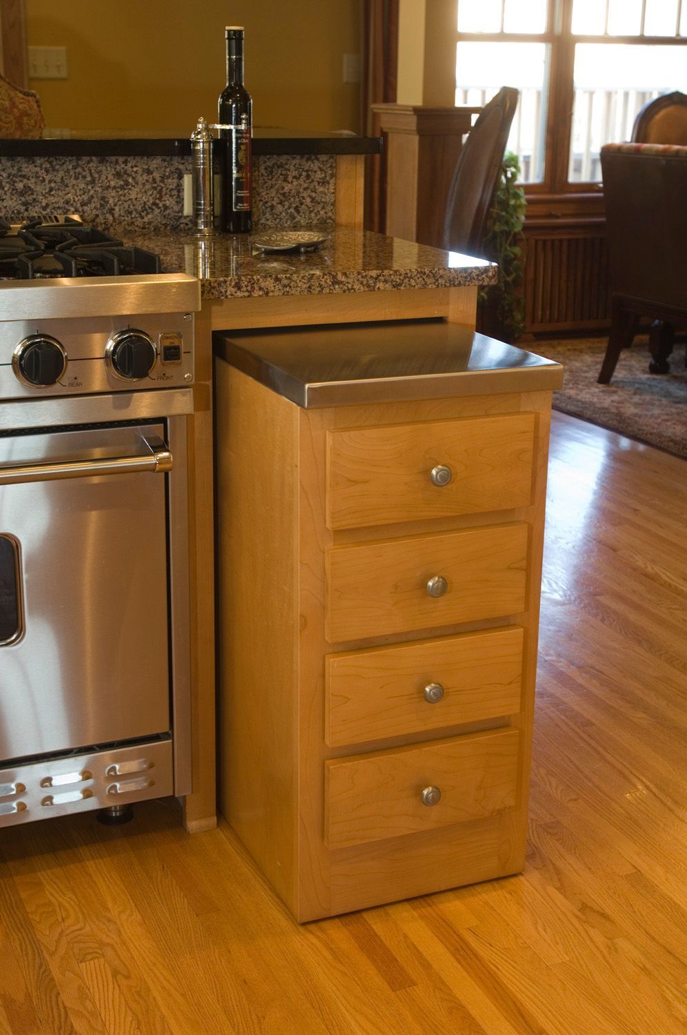 Wooden kitchen cabinet with drawers, stainless steel countertop, next to a stainless steel oven.