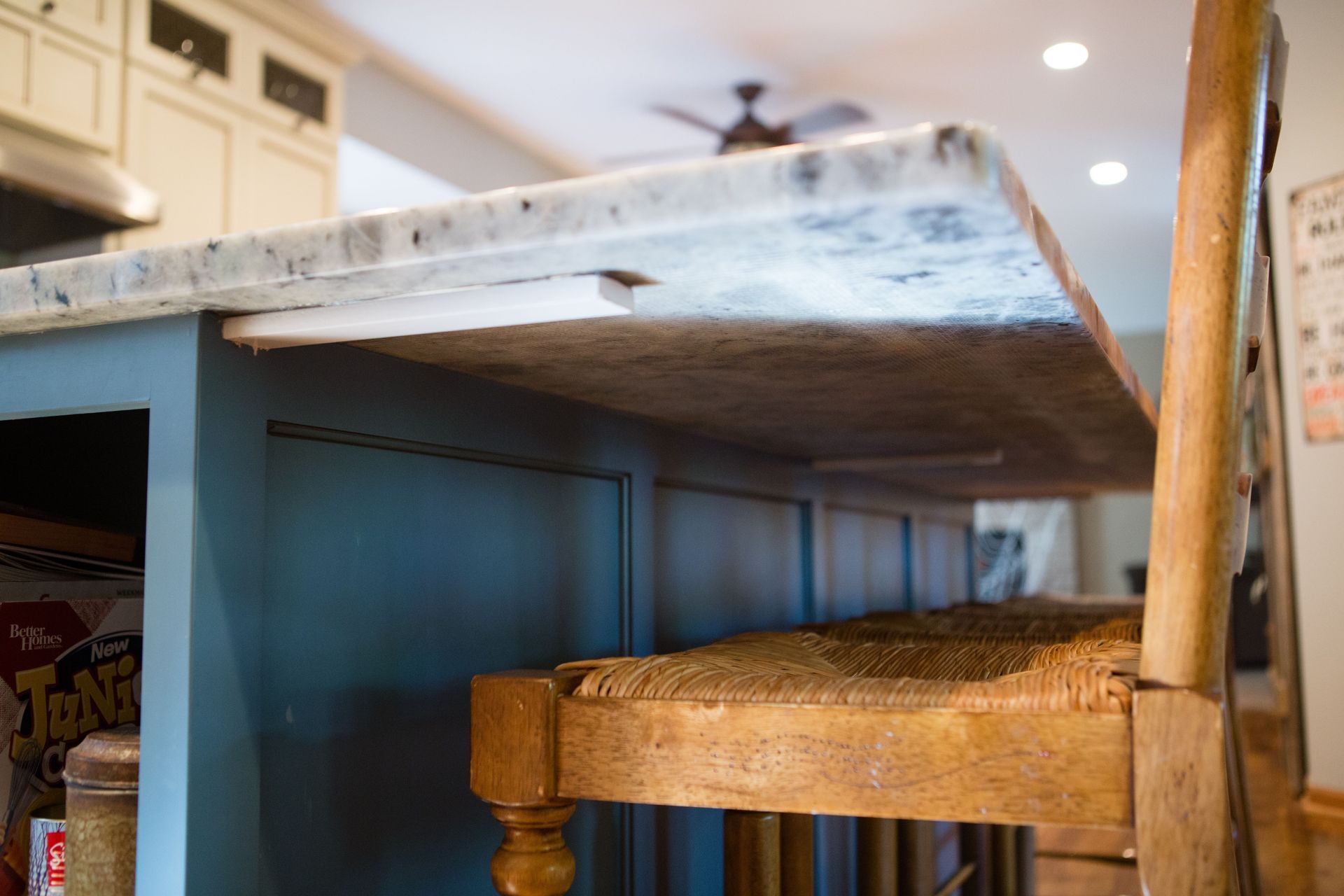 Blue kitchen island with a light-colored countertop. A wooden chair is partially under the overhang.