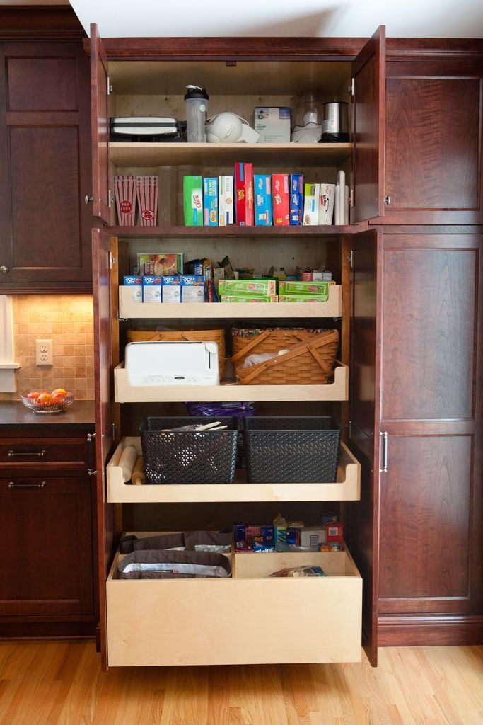 Open kitchen pantry with pull-out shelves filled with food items and baskets, dark wood cabinets.