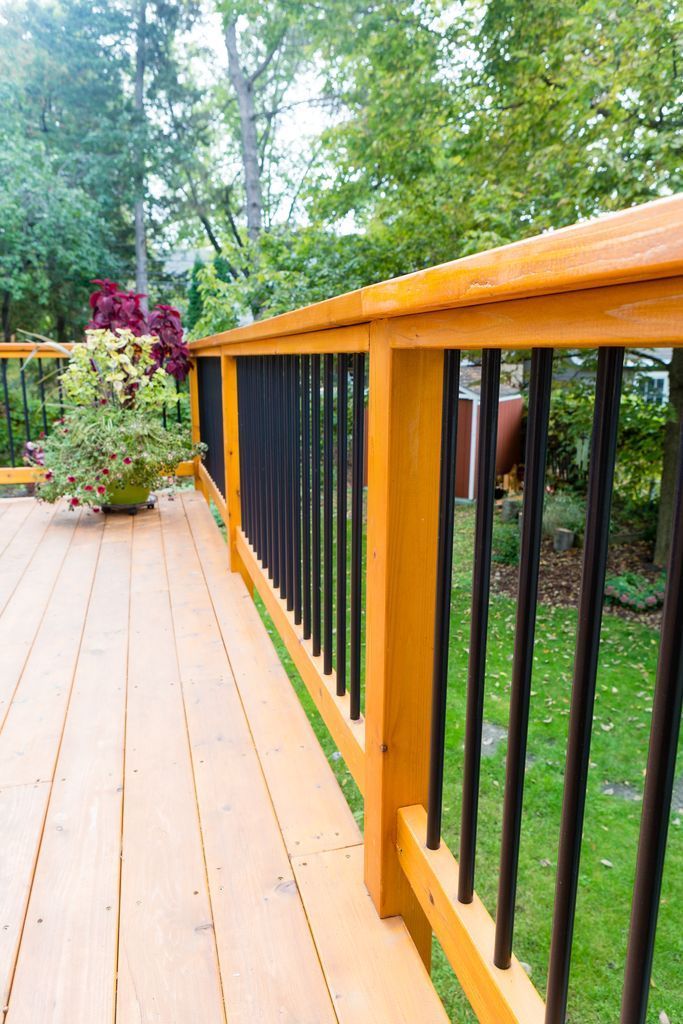 Wooden deck with black railings and potted plants against a backdrop of trees.