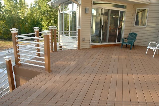 Brown composite deck with white railing and light-colored house, a green and white chair in the background.