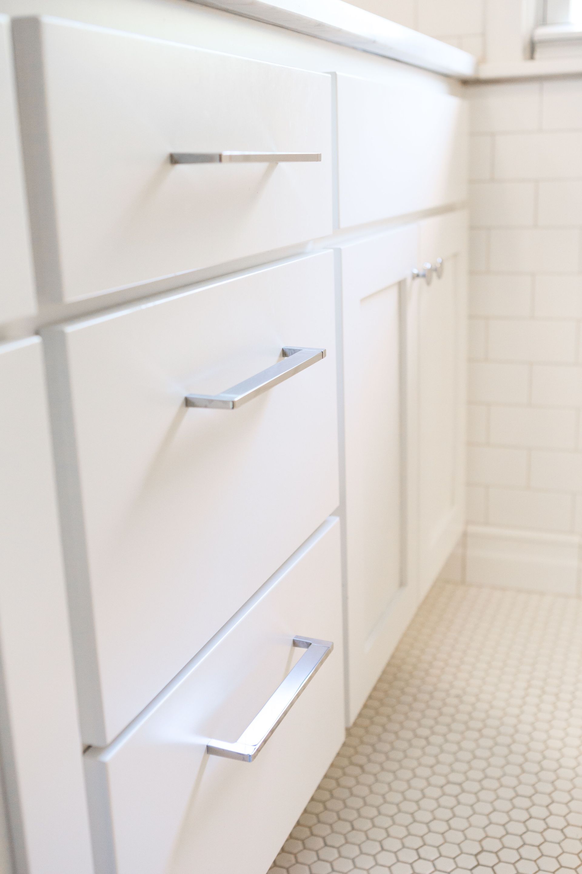 White bathroom vanity with silver handles against white tile.