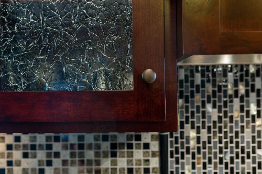 Dark wood cabinet with textured glass, above a mosaic backsplash.
