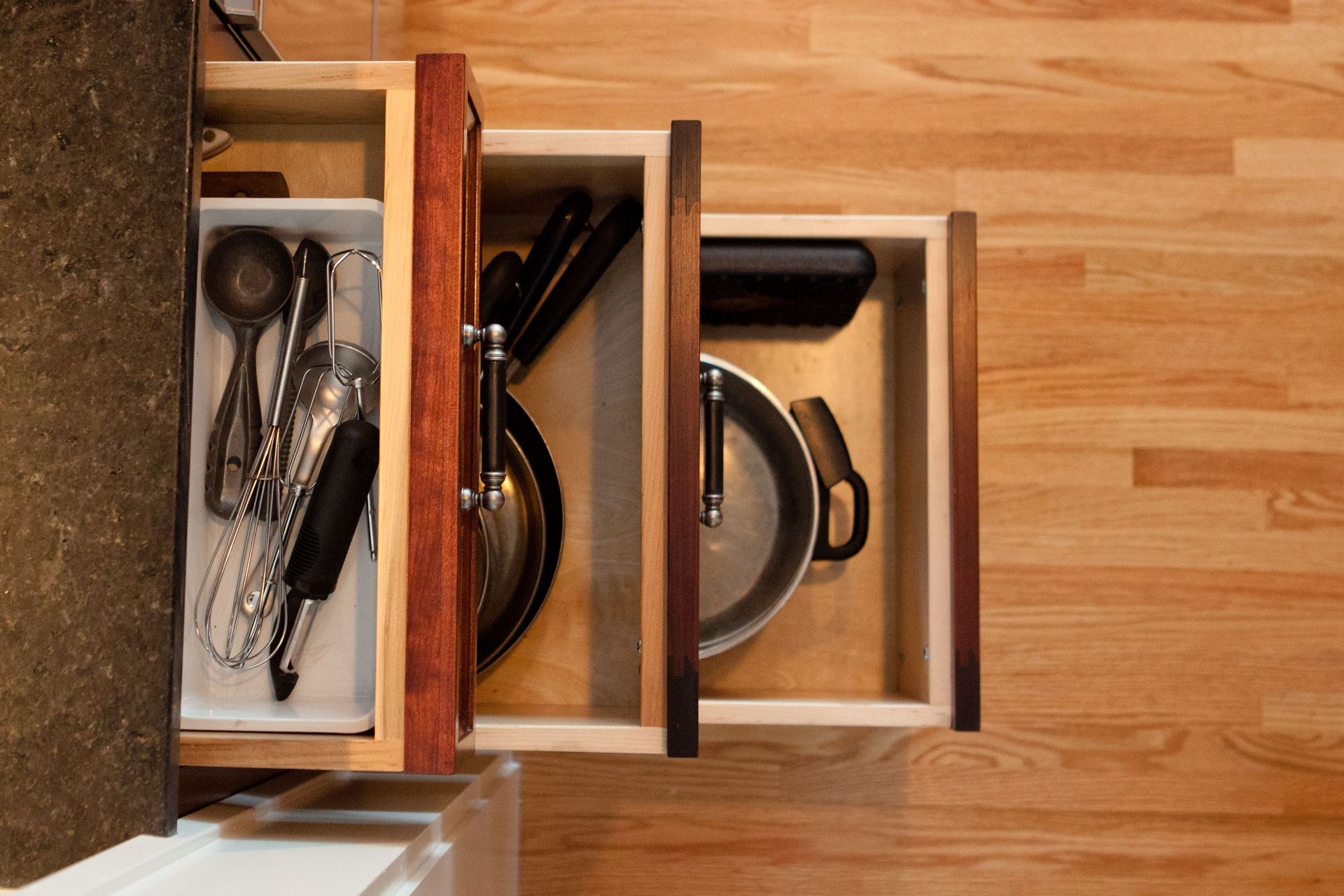 Overhead view of open kitchen drawers: utensils, pans, and a pot stored inside.