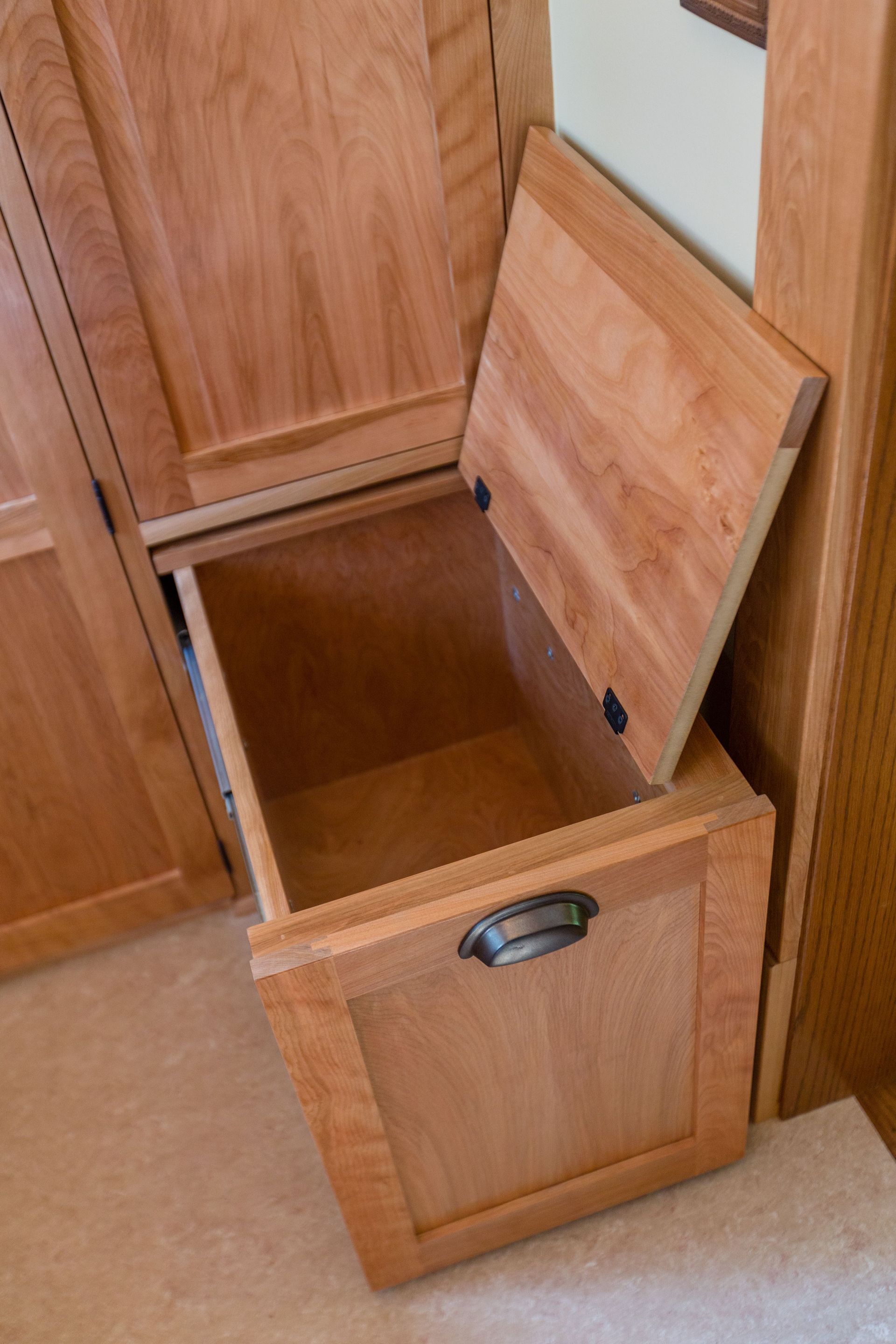 Open wooden storage bin built into a cabinet. Lid up, showing empty interior, metal handle.
