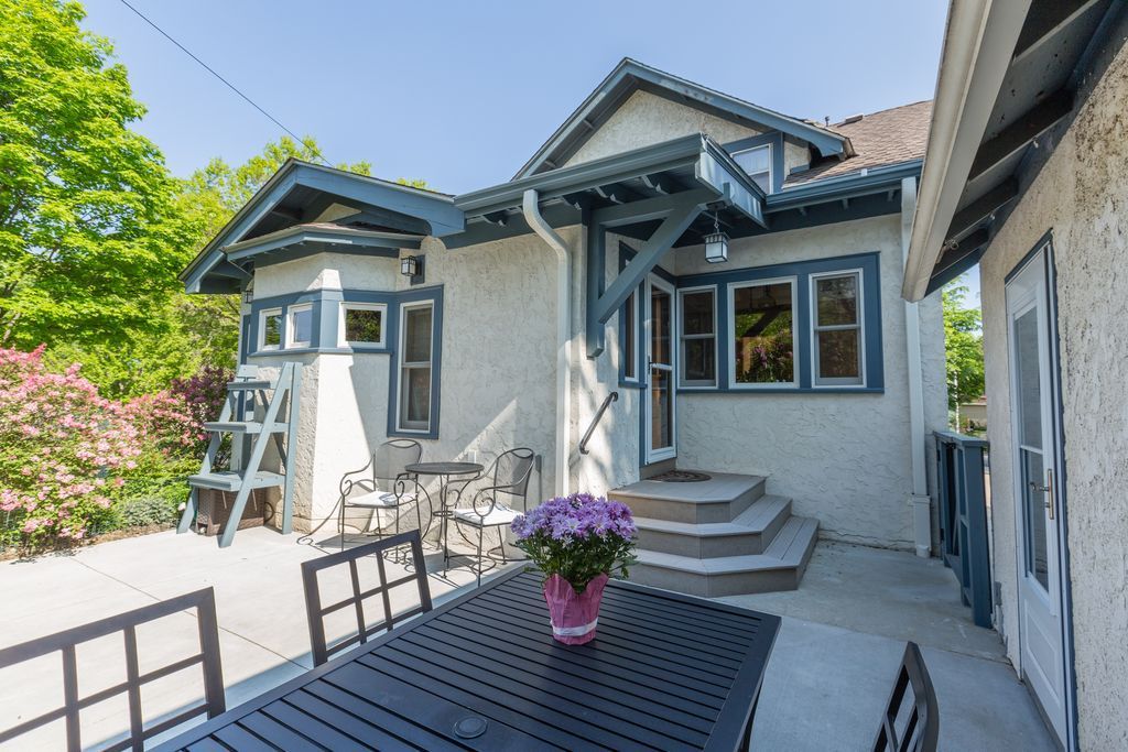 Patio with a black table and chairs, purple flowers, and a white stucco house with blue trim.
