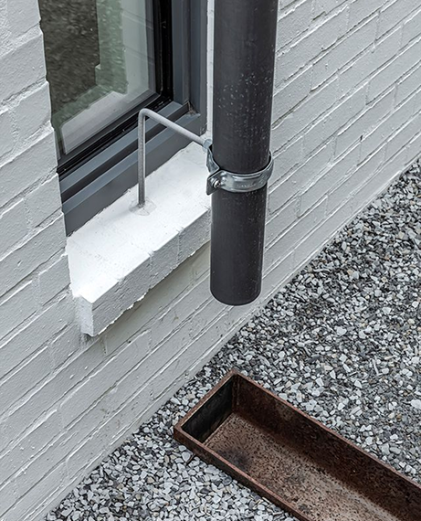 Rain gutter attached to a building's window with a drainage pan on the ground in Little Rock, AR