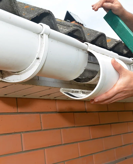 Person attaching a white gutter end piece to a brick house in Cabot, AR.