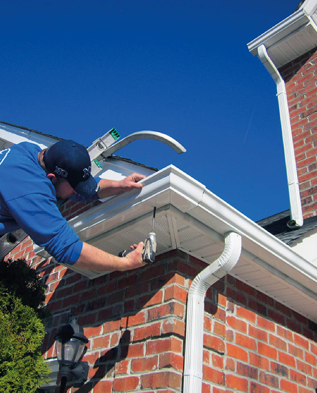 Man installing a white gutter on a Cabot, Ar brick house under a blue sky.