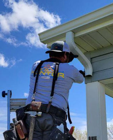 Construction worker on ladder installing gutter downspout on a Cabot, AR house with blue sky background.