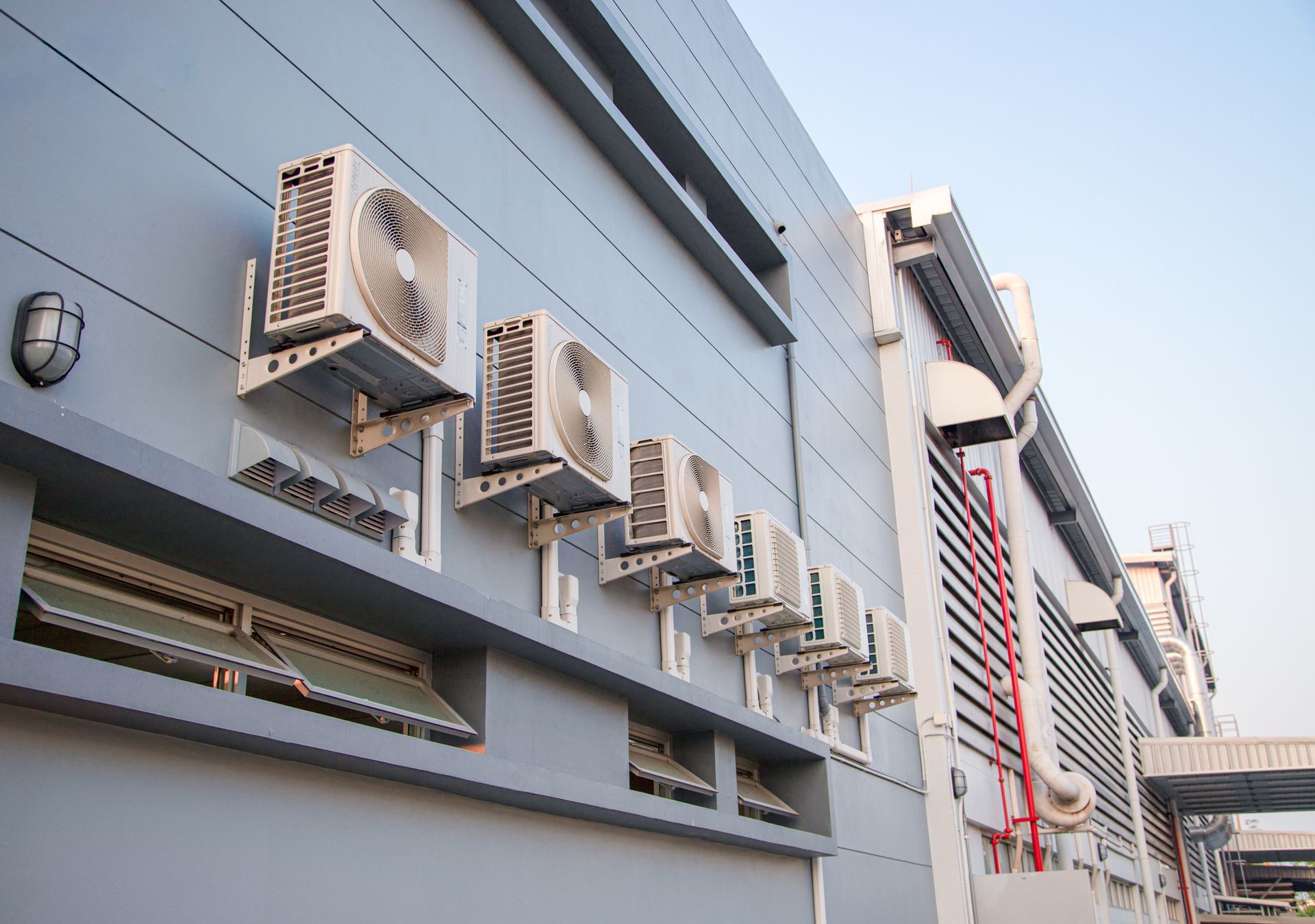 Row of outdoor air conditioner units mounted on a gray building wall along a narrow alley