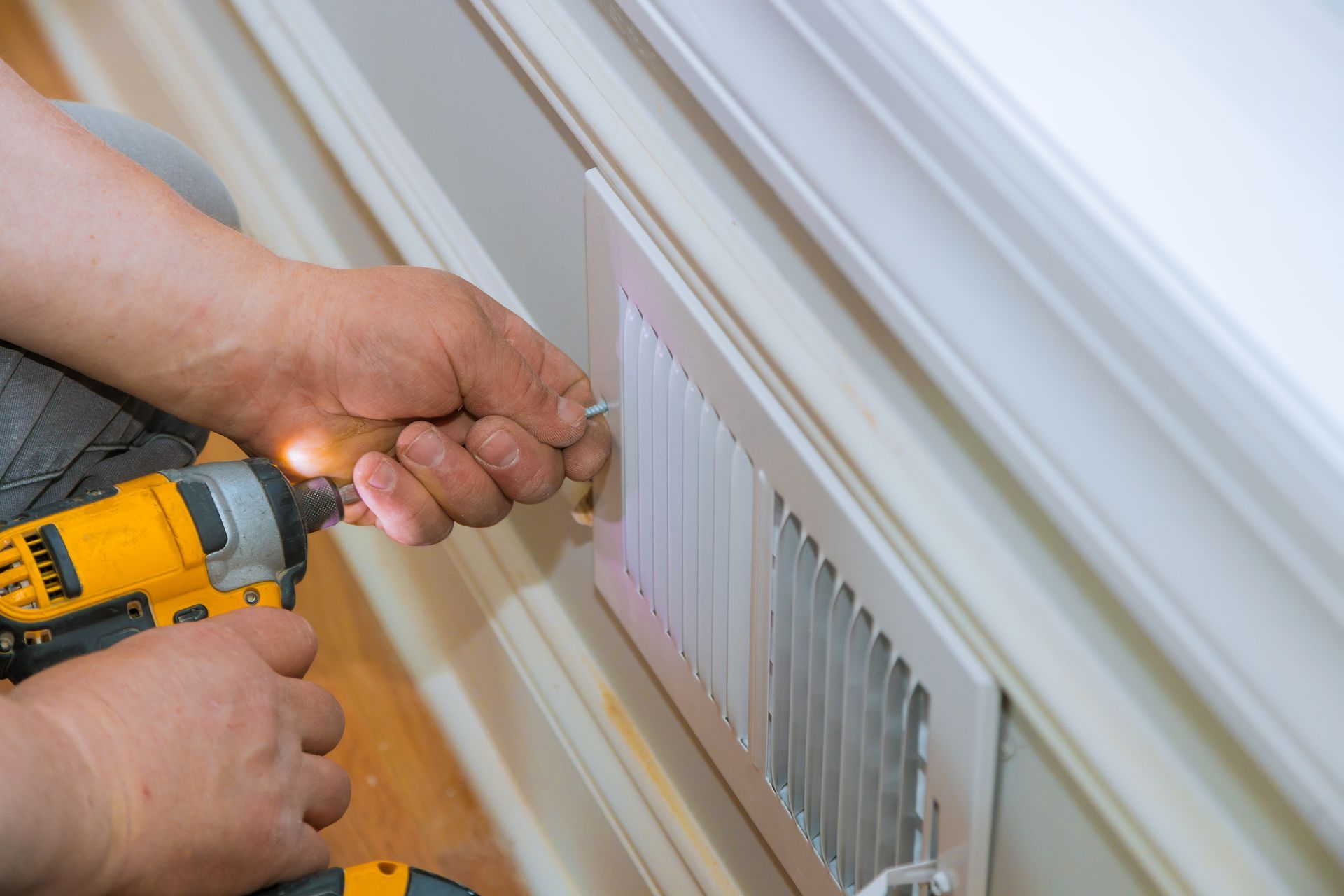 Hands using a drill to install a white radiator cover or trim on a wall