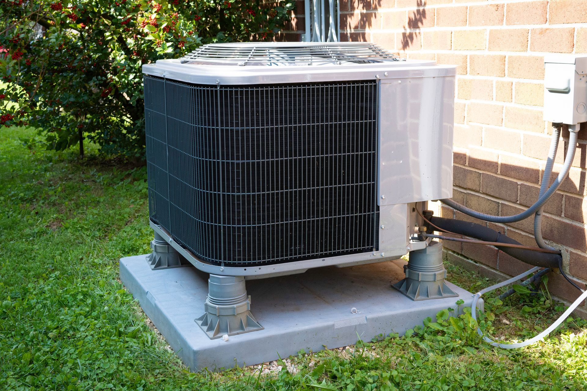 Outdoor air conditioner unit on a concrete pad beside a brick house and grass lawn.