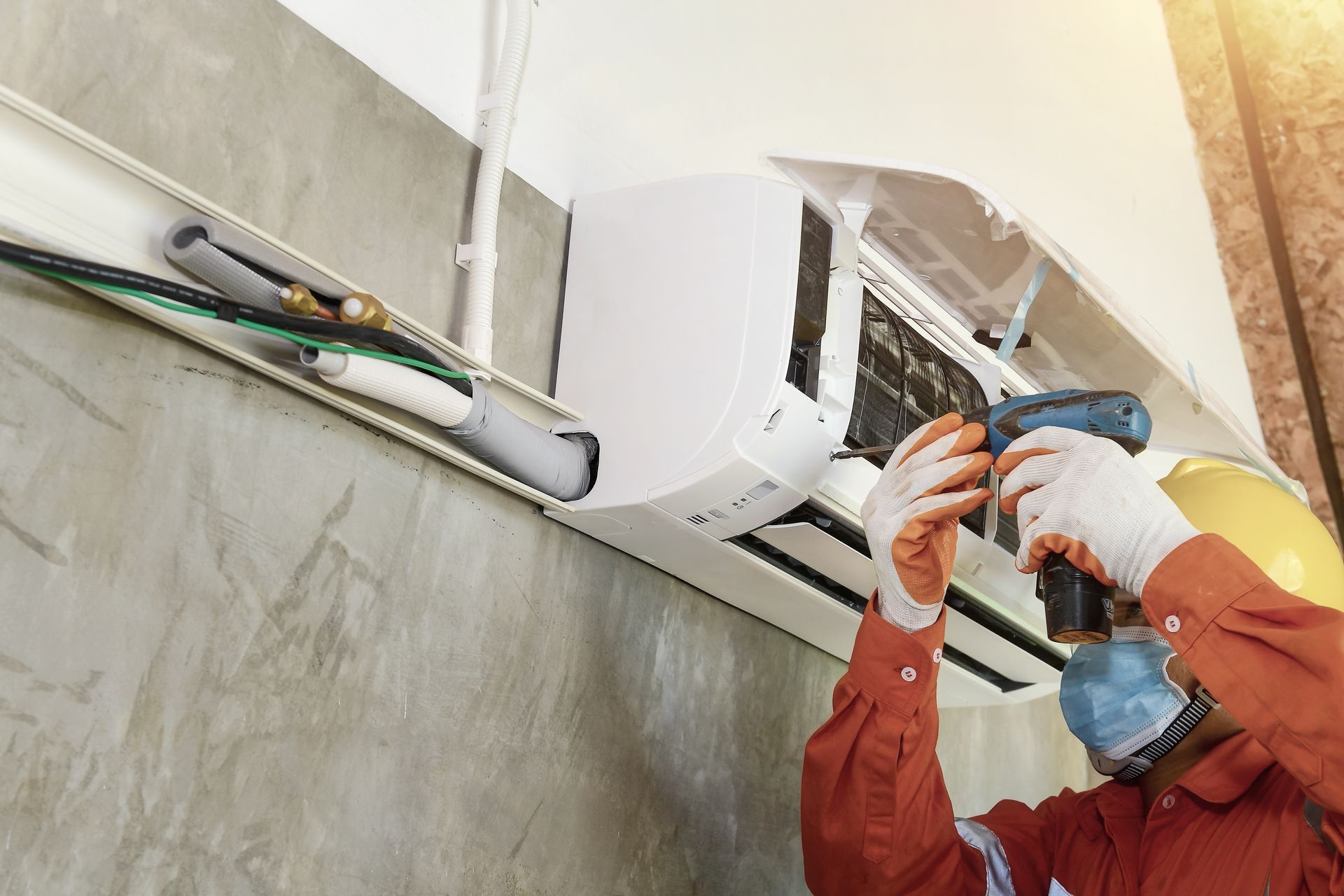 Technician wearing gloves repairs a wall-mounted air conditioner with tools indoors.