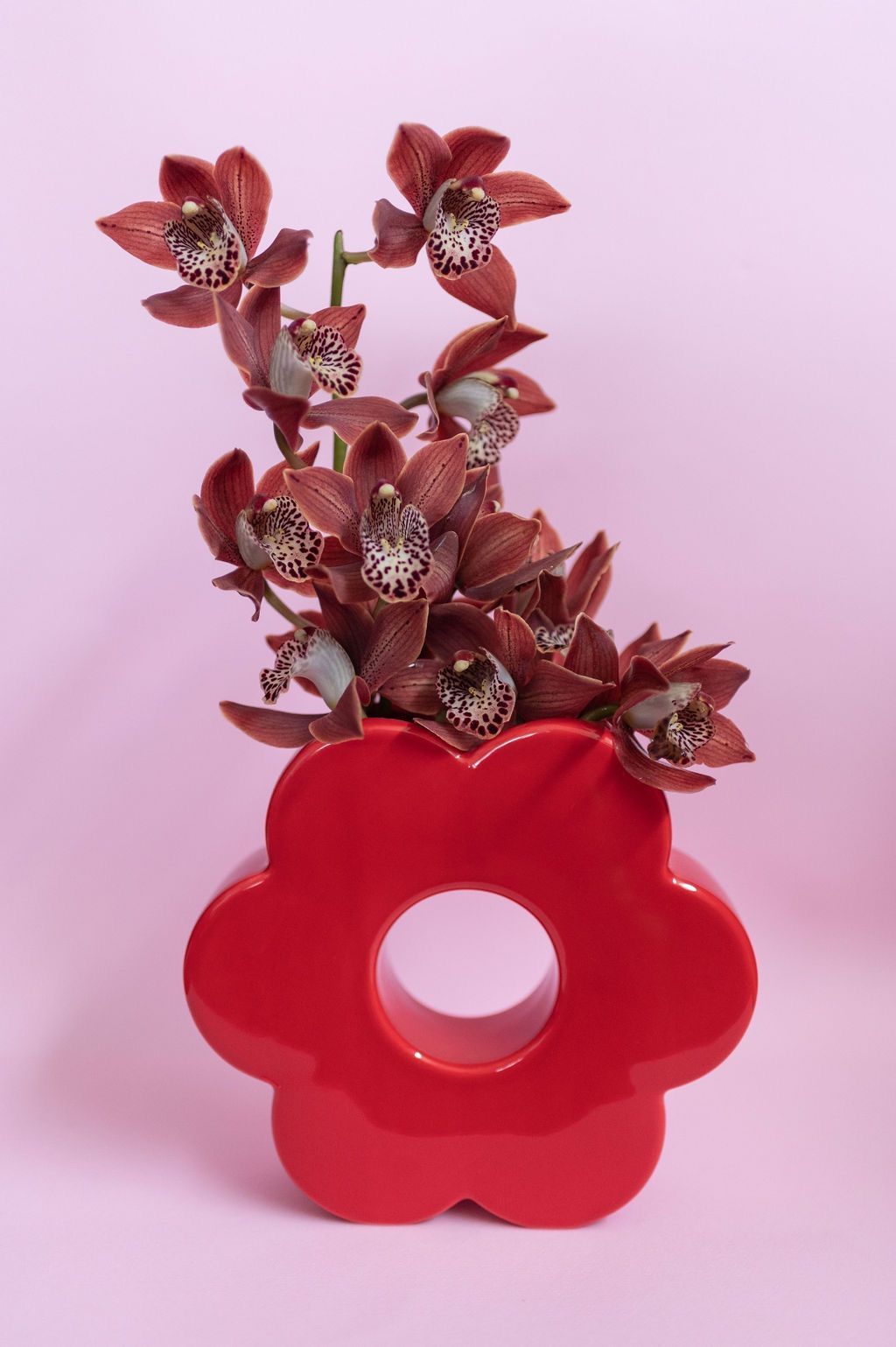 un vaso rosso pieno di fiori su sfondo rosa .