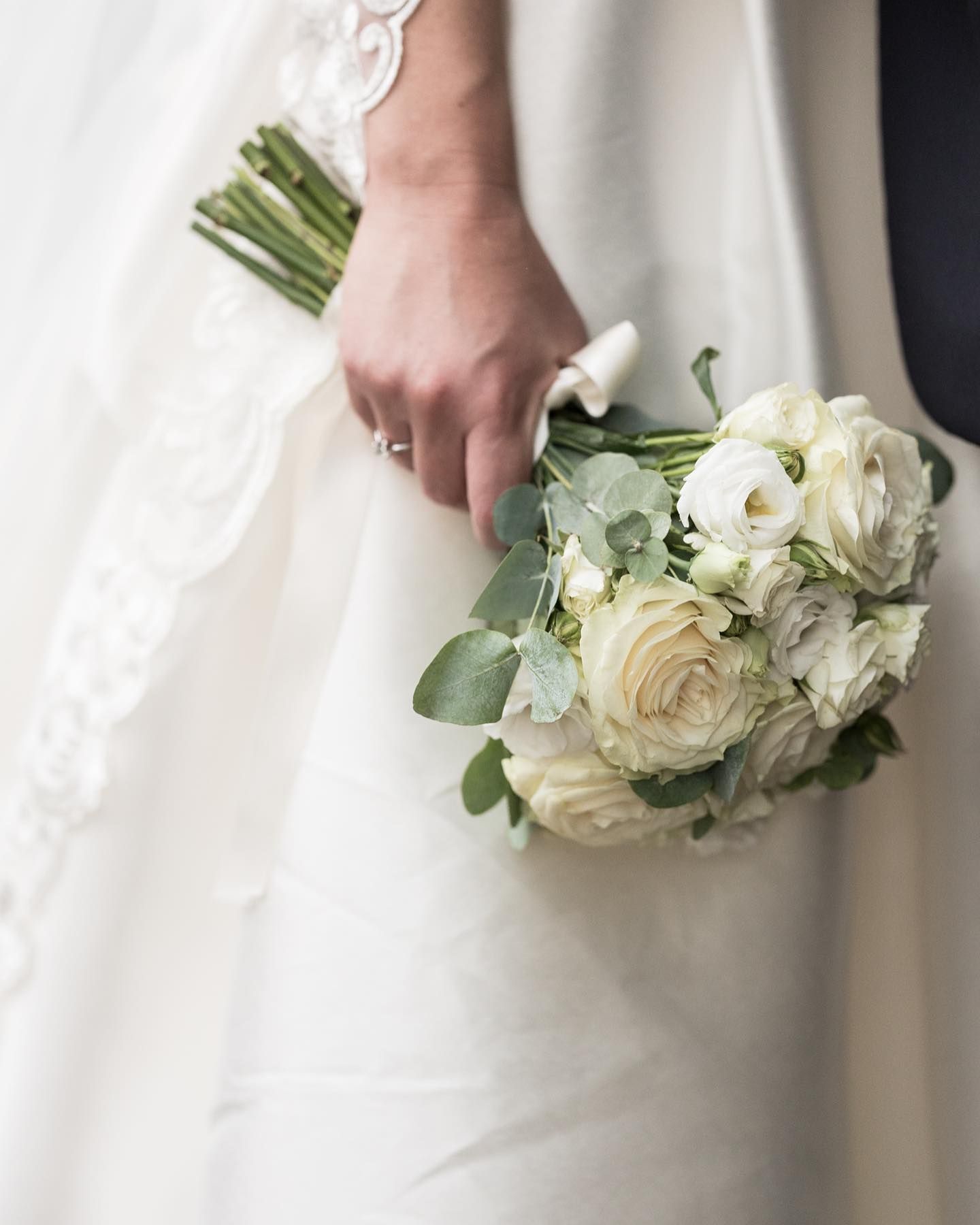 una sposa tiene in mano un bouquet di rose bianche .