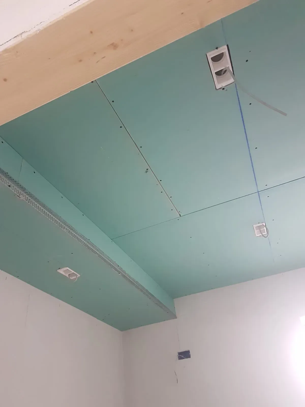 Soffitto in cartongesso blu-verde in costruzione, con scatole elettriche e una trave in legno.
