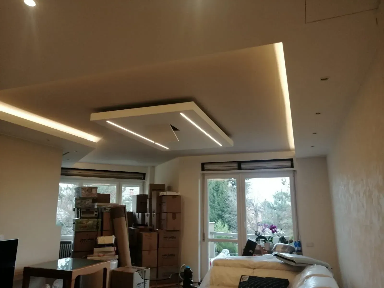 Soggiorno con illuminazione a soffitto, finestre e scatole; colori neutri.