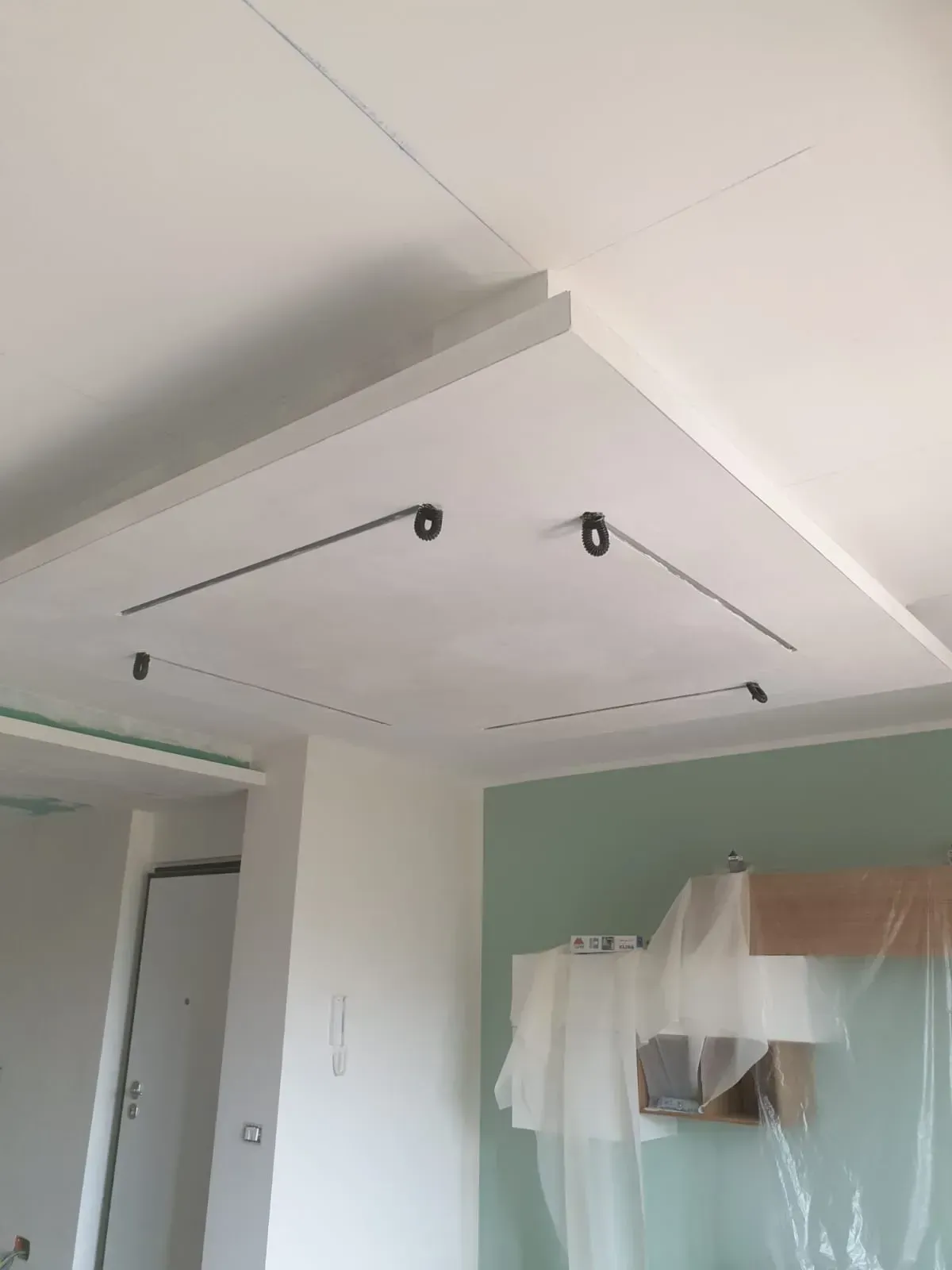 Un soffitto bianco con illuminazione a binario installata in una sezione incassata. Sono visibili una porta e una parete dipinta.