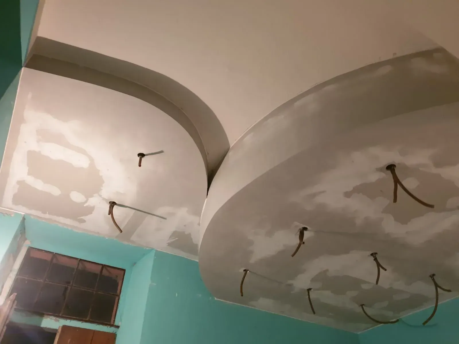 Soffitto bianco curvo con cavi a vista, probabilmente per l'illuminazione, in una stanza con pareti turchesi.