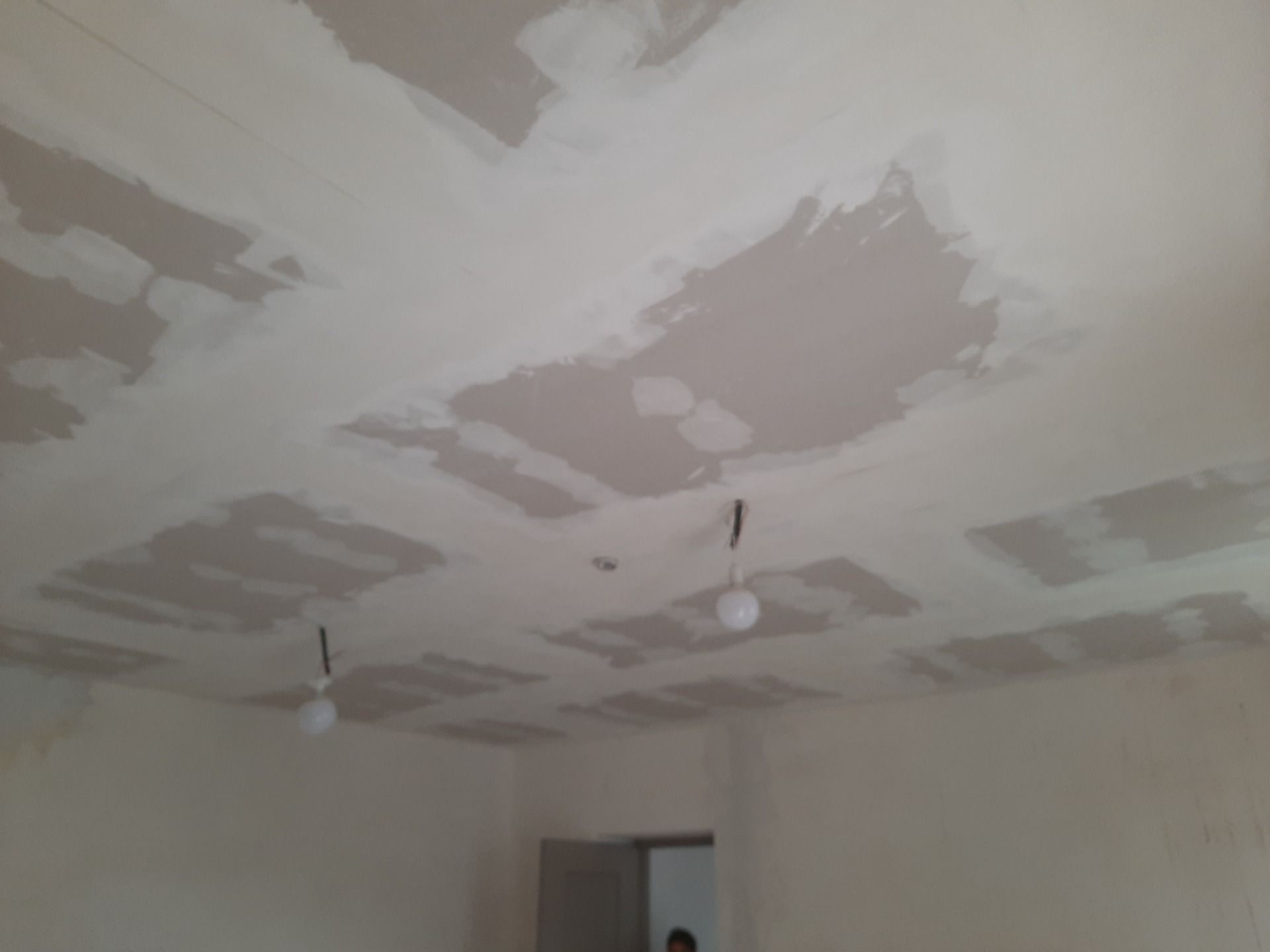 Soffitto con macchie di fango da cartongesso, due lampadine appese, all'interno di una stanza.