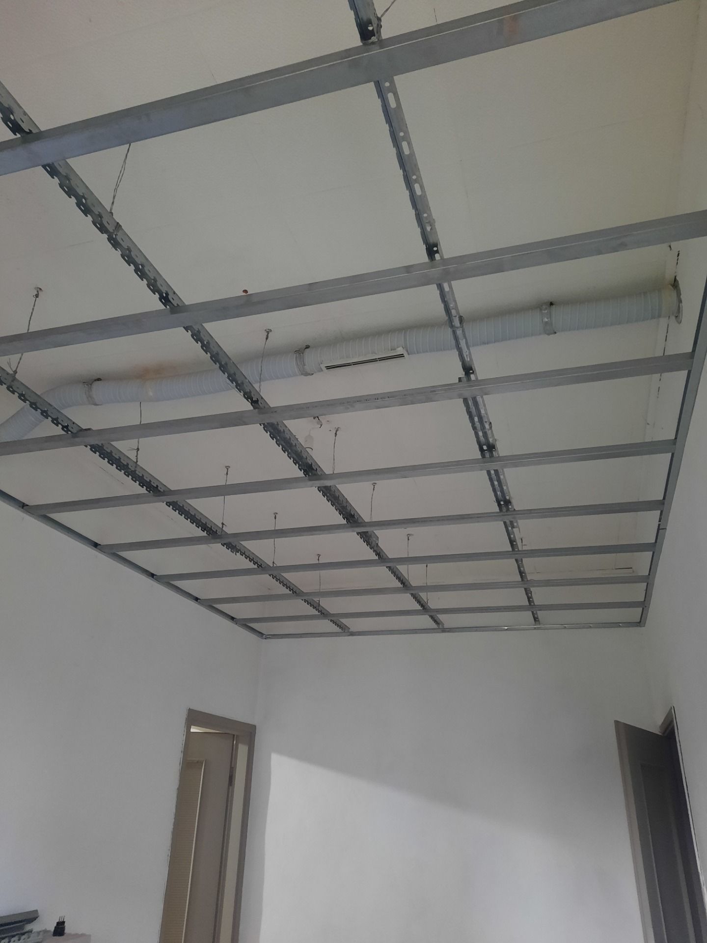Struttura del soffitto con griglie metalliche, sospesa, in una stanza con pareti bianche, pronta per il cartongesso.